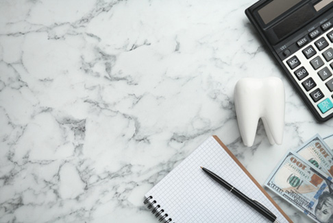 Bird’s eye view of notebook, pen, money, model tooth, and calculator on marbled countertop