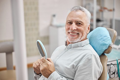 man smiling while holding dental mirror 