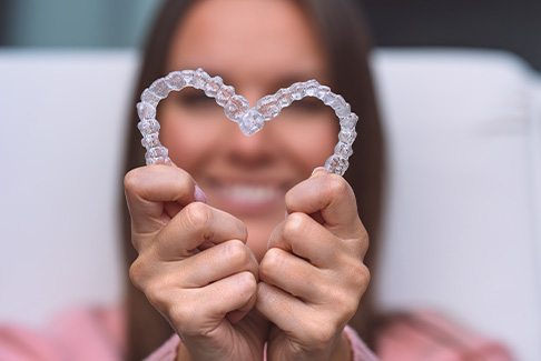 Woman in pink shirt holding clear aligners in the shape of a heart