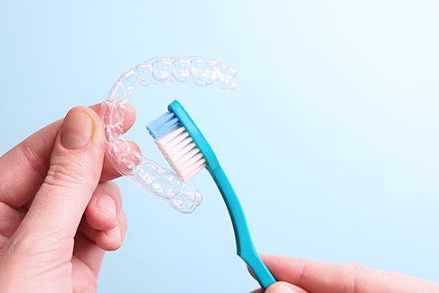 Someone holding teal toothbrush to Invisalign tray with light blue background