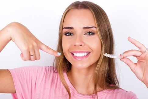 Woman in pink shirt holding Invisalign and pointing to her smile